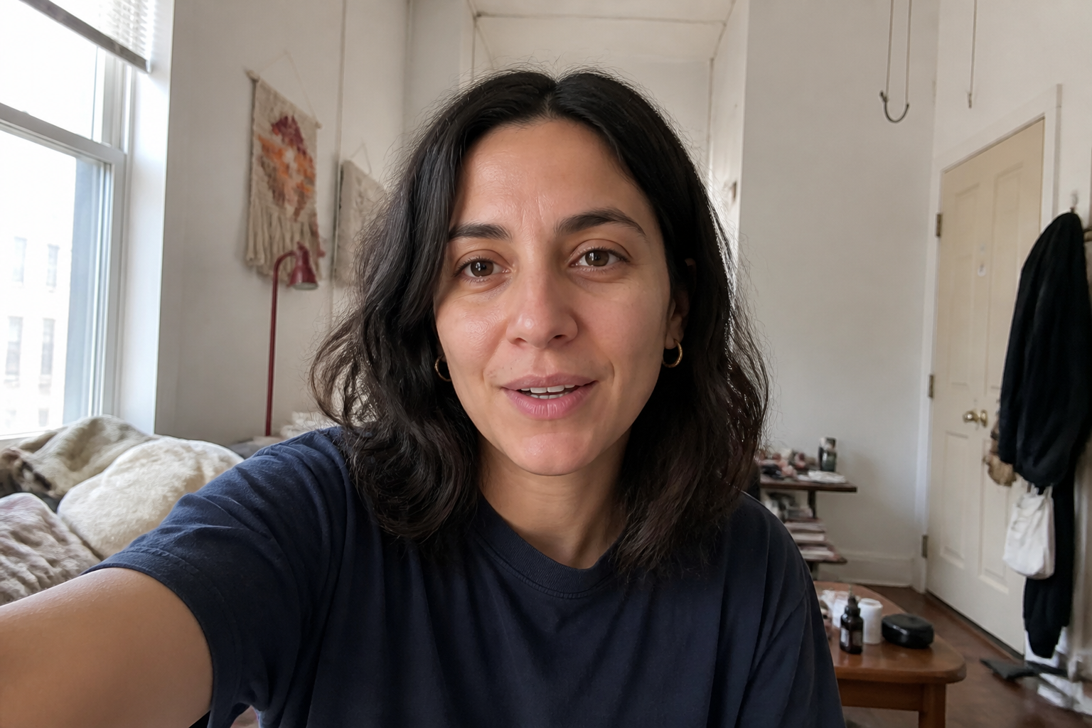 Locked spokesperson: olive skin, dark wavy hair, navy crew-neck, gold hoops, apartment talking-head